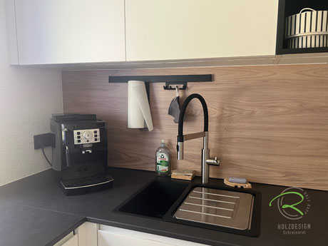 Großzügiges, schwarzes Spülbecken mit mobilem Abtropfblech von Franke für maximale Ausnutzung der Arbeitsfläche, helle Holzdekor Nischenplatte mit schwarzem Relingsystem, Papierrollen Halter und Hakenleiste, darüber weiße Oberschränke 