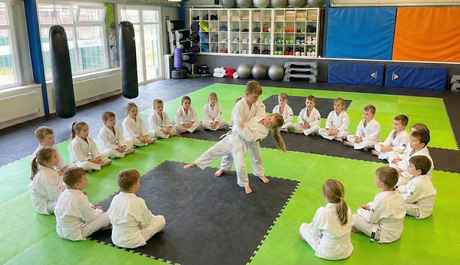zwei Kinder zeigen der Gruppe rund um sich eine Wurftechnik im Kurs Kinder Selbstverteidigung