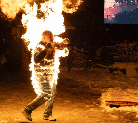 Stuntdarsteller läuft während eines kontrollierten Feuerstunts brennend über eine verschneite Fläche.