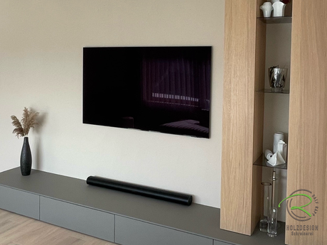 TV Wohnzimmerwand mit Lowboard in grau-braun mit super matter Antifingerprint Beschichtung von Fenix und integrierter Kabeldurchführung für Soundbar und rechts Eiche furnierter Schrankwand mit Anthraziten Glasböden als Verbindung der raumhohen Schränken