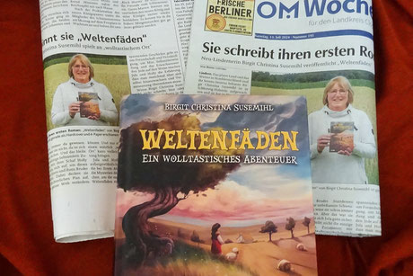 Zwei seitlich gefaltete Zeitungen mit Artikeln über „Weltenfäden“. Beide zeigen das gleiche Foto, auf dem ich das Buch in der Hand halte. Auf den Zeitungen liegt das Buch.