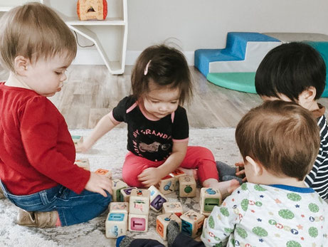 Four toddlers playing with alphabet blocks together on the floor of the toddler room at The Wonder Playschool. 