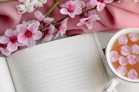 ページが開かれた本と桜の花びらが浮かんだティーカップ。桜の小枝。