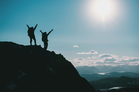 zwei Menschen auf einem Berggipfel mit erhobenen Armen