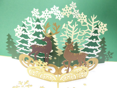 carte de noël en pop-up avec des rennes en forêt de sapin et des flocons autour