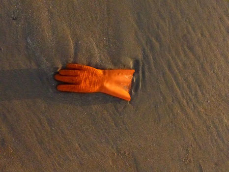 orangener Gummihandschuh liegt am Strand