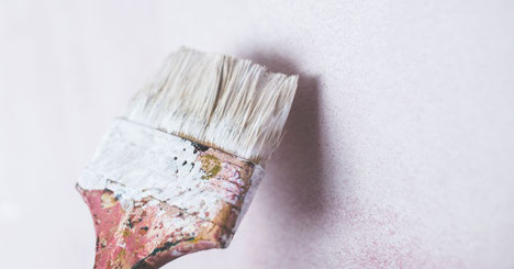 Weiße Wand mit Pinsel mit weißer Farbe, der zum Anstrich ansetzt.