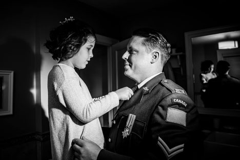 Black and white photo of dad and daughter. Father is in military uniform. Daughter is adjusting father's tie. Reflection is visible in mirror. 