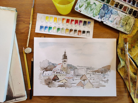 Blick auf Aquarellbild, Dächer eines Dorfes, um das Bild liegen auf einem Tisch Malutensilien
