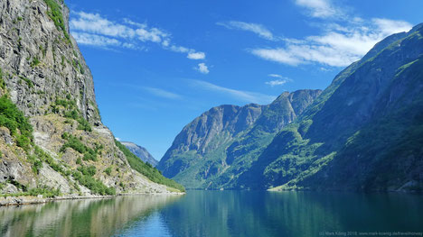 Scenic view from the ferry into the narrow Nærøyfjord with high green and stony mountains on both sides. 