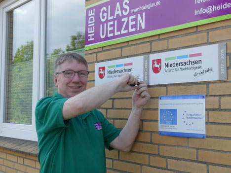 Thorsten Neumann, Inhaber von Heideglas Uelzen, befestigt die neue Kennzeichnung am Firmengebäude.  