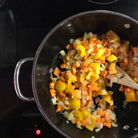 raw carrots, onions and yellow pepper in pan on stovetop