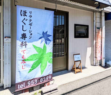 小倉井堀・戸畑のマッサージ・もみほぐし店「ほぐし専科てもみじ」。夏の強い日差しの中で涼やかに揺れる「青い旗」と、外の暑さを忘れて心身を深くリラックスできる、ひんやりと心地よい個室サロンのイメージ。