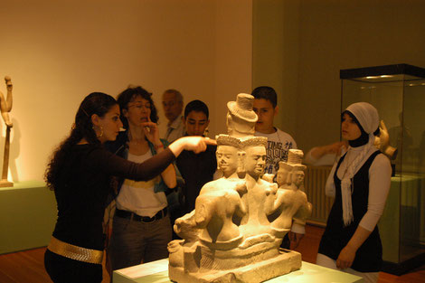 Schülerinnen und Schüler sprechen mit ihrer Lehrerin über eine Skulptur in der Ausstellung „Angkor. Göttliches Erbe Kambodschas“