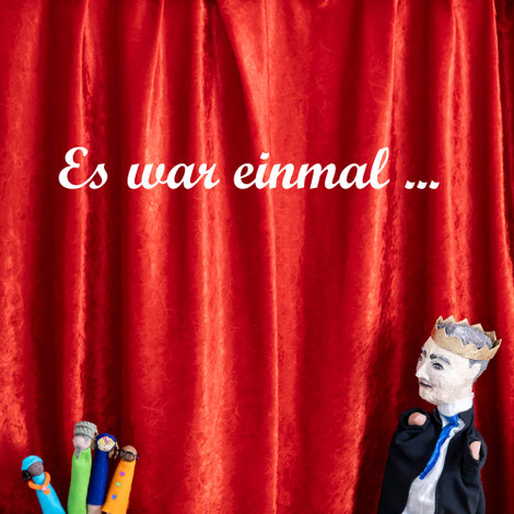 Bild zu Film Es war einmal. Es ist ein Puppentheater mit roten Vorhängen zu sehen. Im Puppentheater ist eine Handpuppe, die der König ist. Der König trägt einen Anzug und eine Krone. Er hä