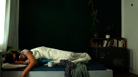 Bild zu Film 625 Tage. Eine Frau liegt mit Augenmaske, Lärmschutz-Kopfhörern und Wärmflasche in einem Bett. Neben ihr stapeln sich schmutziges Geschirr und Wäsche.