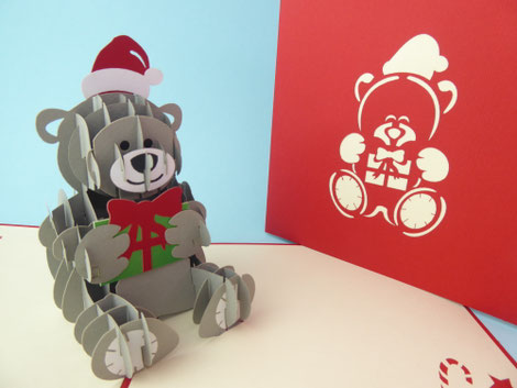 carte de noël en pop up avec un ourson en peluche portant un bonnet de noël et un cadeau