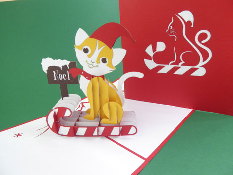 Carte pop-up de noël avec un chat portant un bonnet de noël sur une luge en forme de sucre d'orge