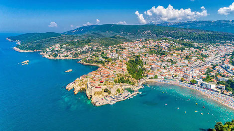 Aerial panorama of Ulcinj, Montenegro showing the historic Old Town peninsula, turquoise Adriatic Sea, Small Beach, and surrounding coastline with mountains in the background