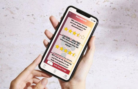 Hände halten ein Smartphone. Es ist eine geöffnete Event-App zu sehen, in der Feedback zu einem Event übermittelt werden kann.