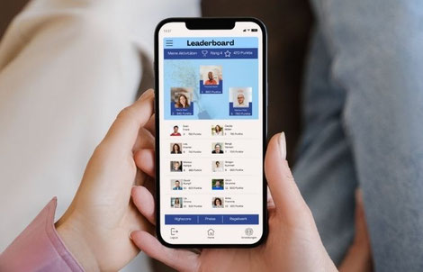 Zwei Personen sitzen nebeneinander und schauen auf ein Smartphone. Man sieht eine geöffnete Event-App, bei der die Gamification-Sparte geöffnet ist. Man kann das Leaderboard für die Veranstaltung erkennen.