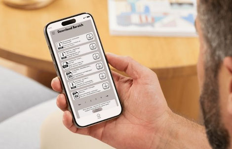 Eine Person sitzt an einem Tisch und hält ein Smartphone in der Hand. Auf dem Smartphone ist eine Event-App geöffnet und der Download-Bereich zu dem Event ist zu sehen.