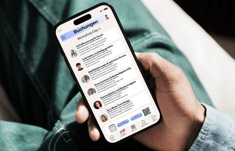 Eine Person sitzt auf einem Stuhl und hält ein Smartphone in der Hand. Auf dem Display ist eine Event-App zu sehen, bei der man Buchungen für ein Event vornehmen kann.