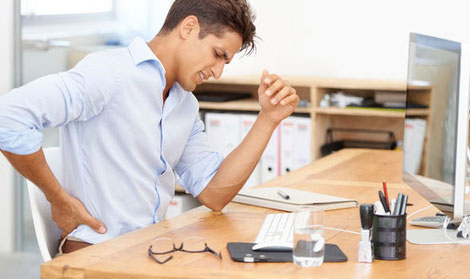 An Indian male executive seated on his desk suffering from back pain at his work desk