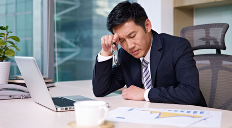 A male Singaporean executive sitting at his desk with his hand on his forehead frowning