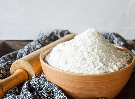 A bowl of refined white flour and bread roller that sits on a crunched up next to a roller and table cloth 