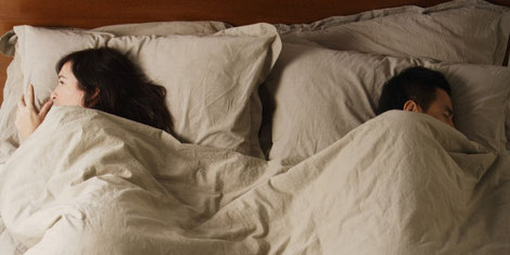 A picture of an asian couple disconnected, sleeping at the opposite ends of the bed