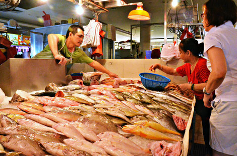 A fish monger selling fish to two Singaporean ladies at a local wet market