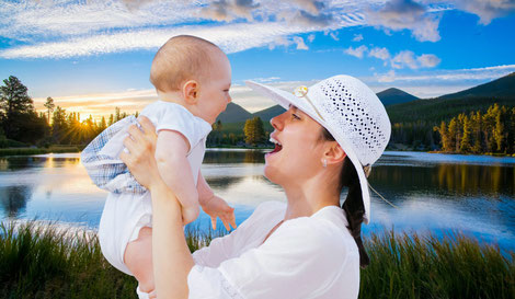 Strahlende Mutter die ihr kleines Baby hochhält und anlächelt.