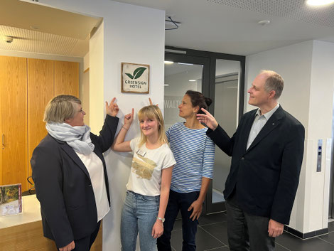 Rezeptionsleiterin Stefanie Siebert, Mitarbeiterin Jasmin Zahner, Bildungsreferentin Nicole Garos und der ­Direktor der Bildungshäuser, Professor Elmar Koziel, deuten auf das Greensign im Eingangsbereich der Rezeption des Diözesanhauses. Foto: C Gahlau