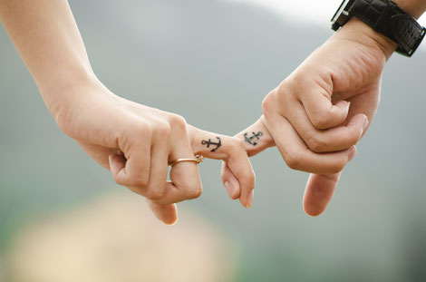 Un homme est une femme se tiennent par l'index. Ils ont tous deux un tatouage représentant une ancre marine sur la tranche du doigt