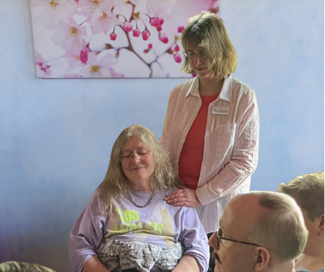 Ina Paulus legt während einer Heilsession einer sitzenden Klientin eine Hand auf die Schulter und eine Hand auf den Rücken