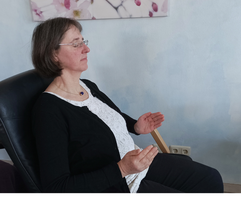 Geistheilerin Ina Paulus sitzt in einem Sessel, hält die Hände auseinander und sendet damit Heilenergien während einer Fernheilung zu einem Klienten