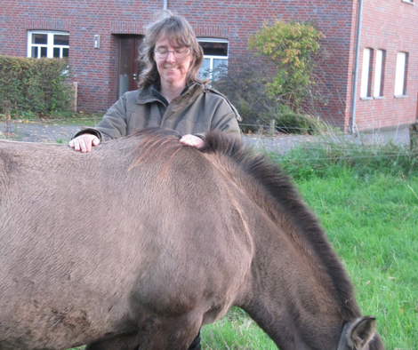Ina Paulus steht mit einer Konikstute auf euner Wiese und legt dem Pferd die Hände während einer Heilsitzung auf den Rücken