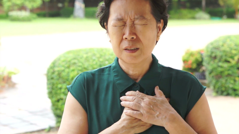 An asian senior woman frowning whilst she places both her hands to her heart in pain