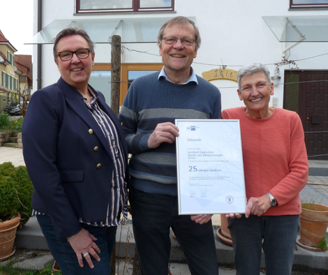 Gruppenbild mit drei Personen, zwei halten eine Urkunde im Bilderrahmen in die Kamera