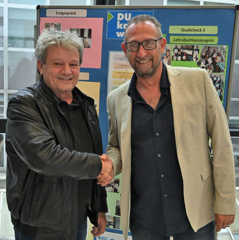 Zwei Männer geben sich die Hand vor einem Poster zum Projekt "Du kannst was".