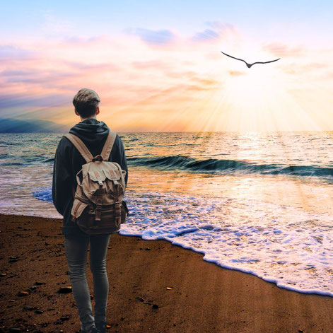 Mann mit Rucksack am Meer mit Blick auf einen Vogel, der in die Sonne fliegt