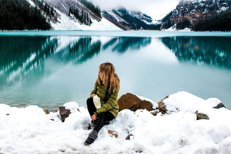 Frau sitzt im Winter am Ufer von einem Bergsee