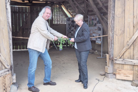 Roland Meyer und Jutta Wendland-Park stehen vor dem Eingang zum Schafstall und zerschneiden ein geschmücktes Band.