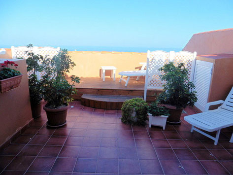 Große geflieste Terrasse mit Gartenmöbel und Pflanzen, sowie Blick auf das Meer.
