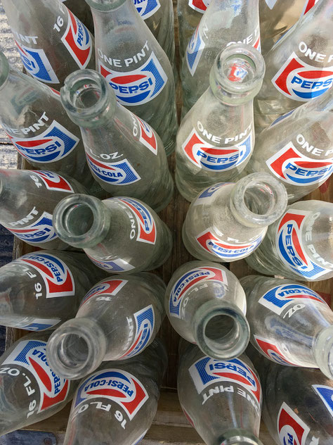 Empty vintage Pepsi glass bottles are arranged upright in a wooden crate, viewed from above.