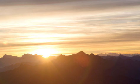 Color photo of the sun at dawn peeking over the mountain tops on the horizon