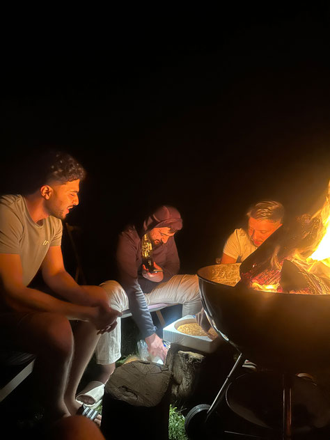 Teilnehmende des Integrationsprojekts Wanderglück sitzen am Abend gemeinsam am Lagerfeuer vor der Selbstversorgerhütte im Allgäu und verbringen Zeit miteinander.