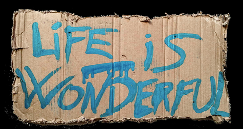 Sur un bout de carton aux bords déchirés un slogan en peinture bleue claire avec quelques coulées dit: Life is wonderful série de Philippe Echaroux sur la mise en valeur de l'handicap.