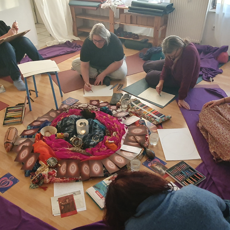 Frauen sitzen im Kreis und zeichnen im Frauenkreis ihre Heilungsbilder in Mainz Laubenheim. In der Mitte befindet sich ein reich geschmückter Altar.